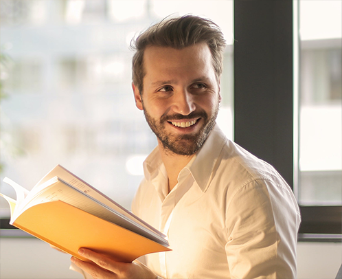 A close up of a professional man smiling and looking at someone off camera with an open journal in his hands